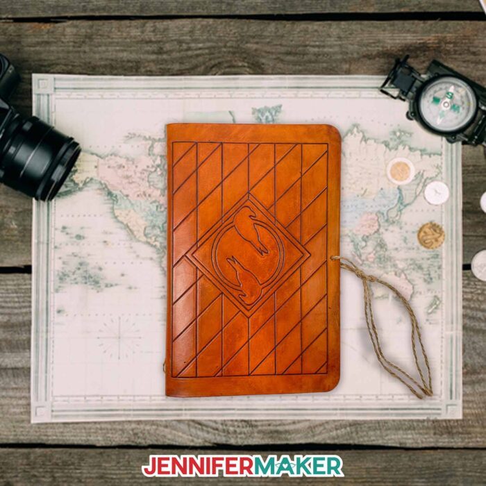 A DIY leather journal in brown with decorative engraved line designs and two ravens on a desk.