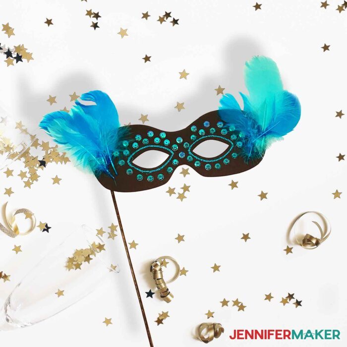 DIY Masquerade Mask with a black and blue feathered mask dowel holder on a party background