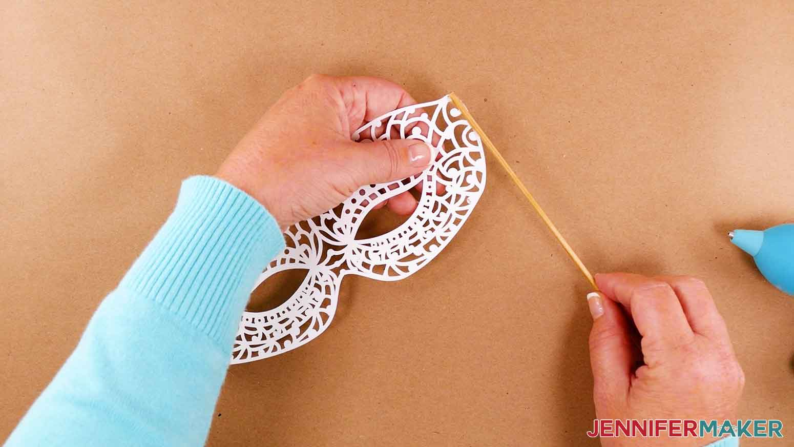 Use hot glue to adhere wooden dowel to masquerade mask.