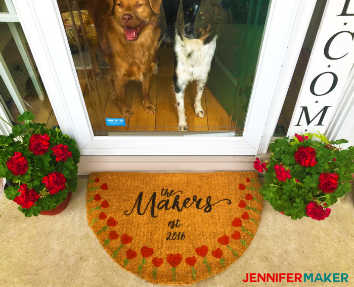 A DIY painted and personalized door mat in front of a house door with my two cute dogs