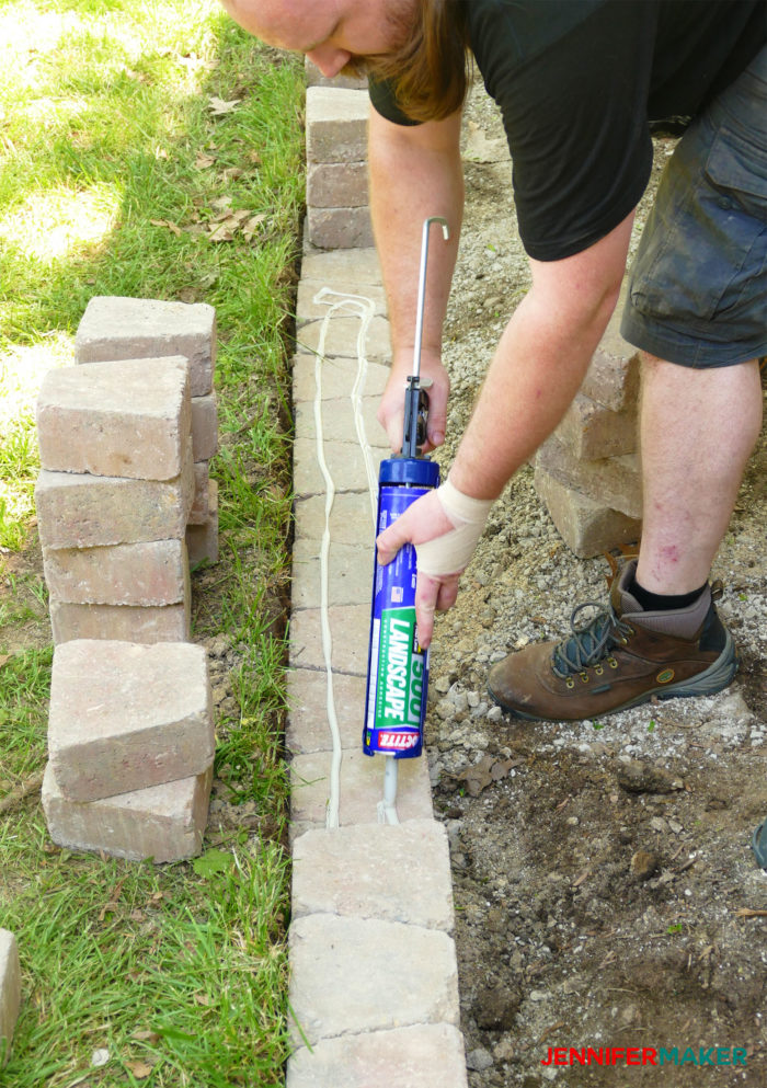 Putting construction adhesive on bricks to make a retaining wall