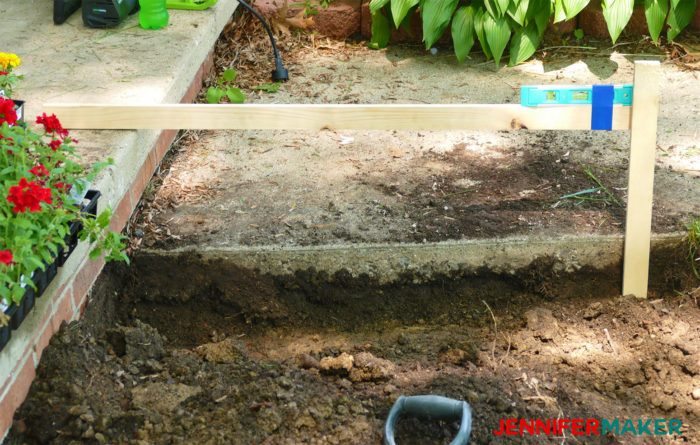 Measure the depth of a our dirt trench with a level and a stick to build DIY retaining walls