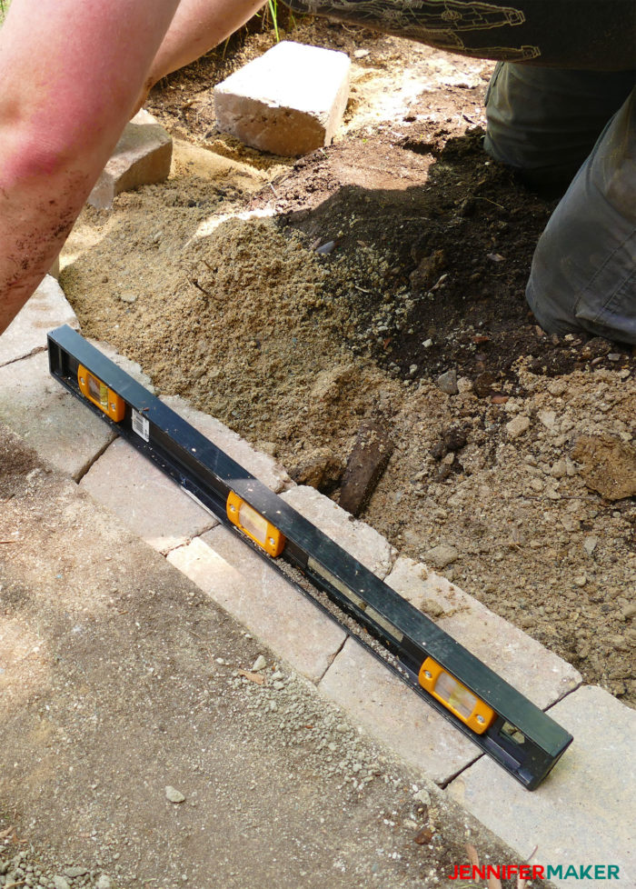 Placing the first course of bricks using a level to keep a straight DIY retaining wall