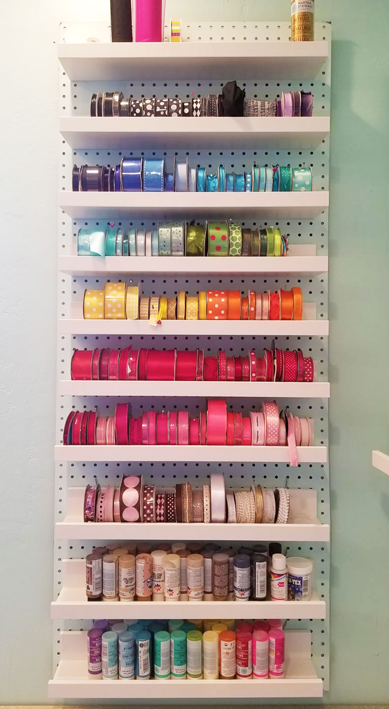 Ribbon storage on a wall: ribbon spools can be put on shelves on a pegboard to organize them! #craftroom #storage #organization