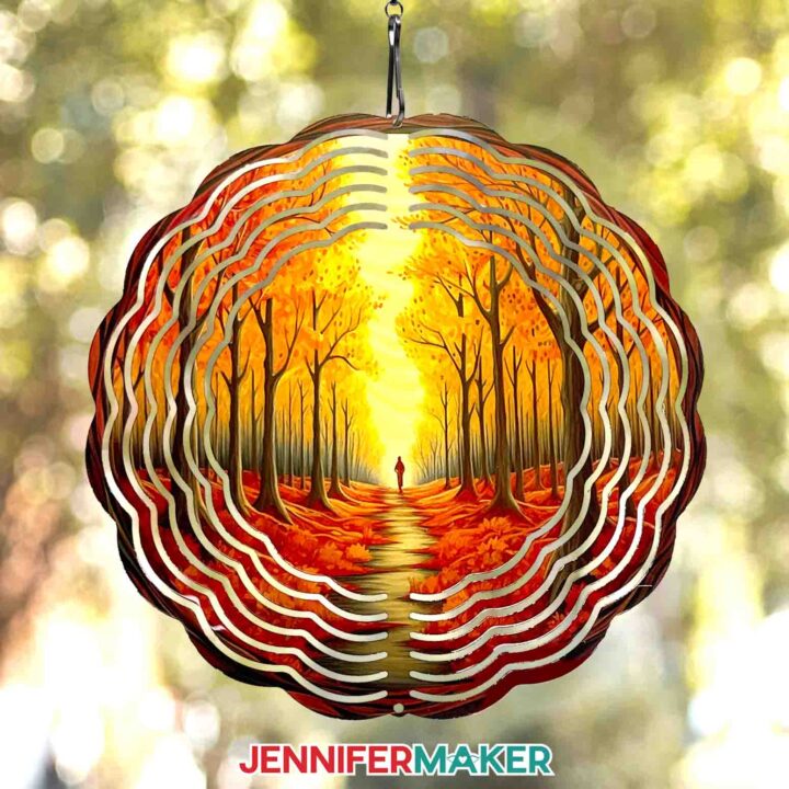 Learn how to sublimate a wind spinner with JenniferMaker's tutorial! A vibrant sublimated wind spinner hangs outdoors, printed with a beautiful orange and brown-toned autumn woods scene.