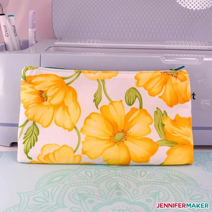 DIY Zipper Pouch with yellow flowers in front of a Cricut Maker cutting machine 