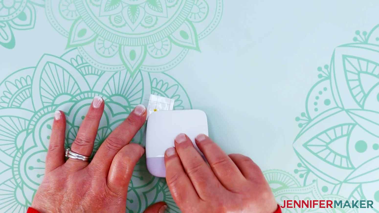 The crafter is using her small scraper to burnish transfer tape to layer vinyl for Dollar Tree Cricut Projects.