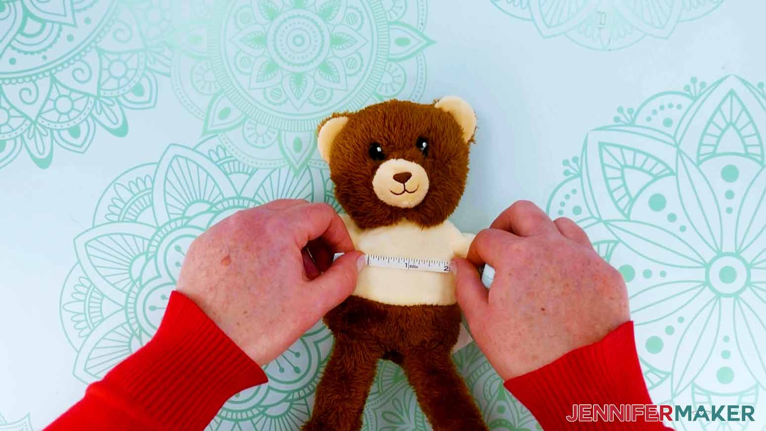 The crafter is using a ruler to measure the dimensions of the stuffed bear's shirt.