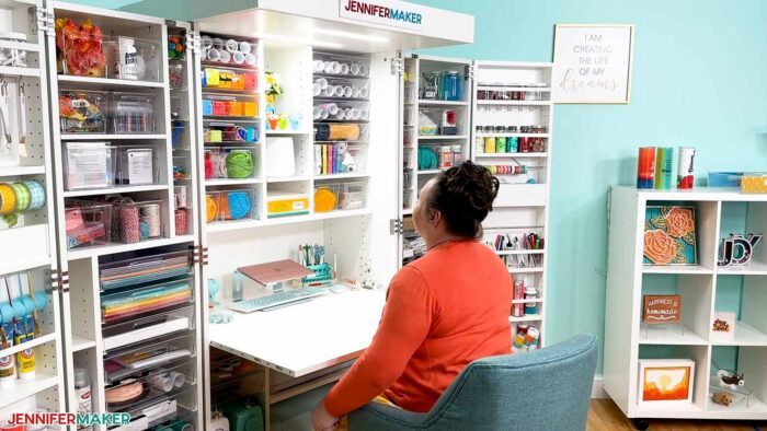 Jennifer Maker sitting at the fold out table on her DreamBox 2 craft storage furniture surrounded by organized craft supplies.