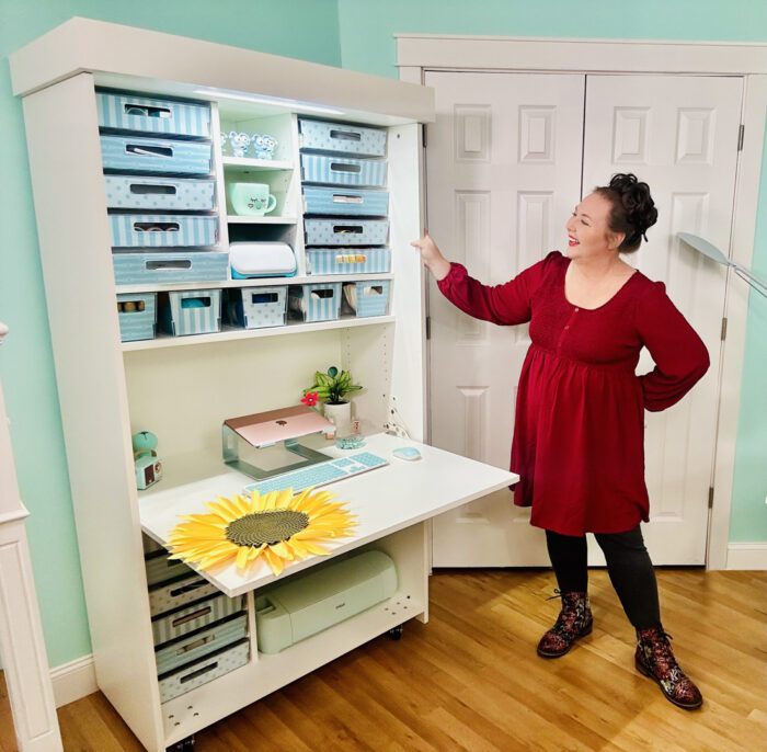 Jennifer Maker shows off the Dreambox Center with the center table extended and colorful storage totes and Cricut machines on the shelves.