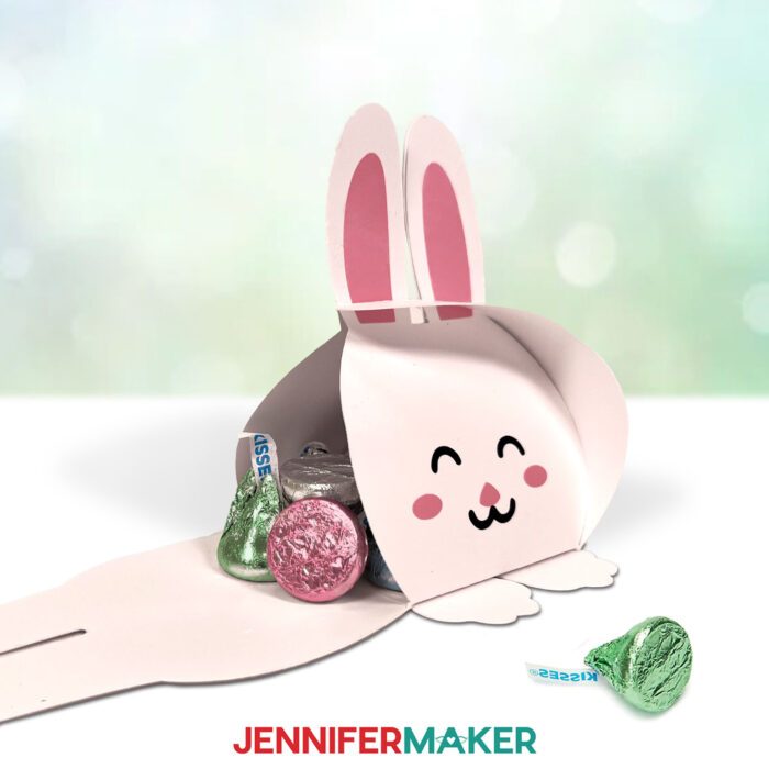 One of the Easter Treat Boxes, a white bunny design, sits with one of its sides open, foil wrapped chocolate kisses spilling out from the inside 