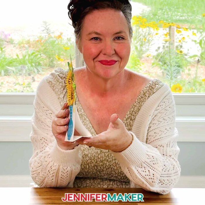 Jennifer Maker sits at her craft table, holding the Easy 3D Bouquet Card from the side, showing off its functional built-in cardstock base for display