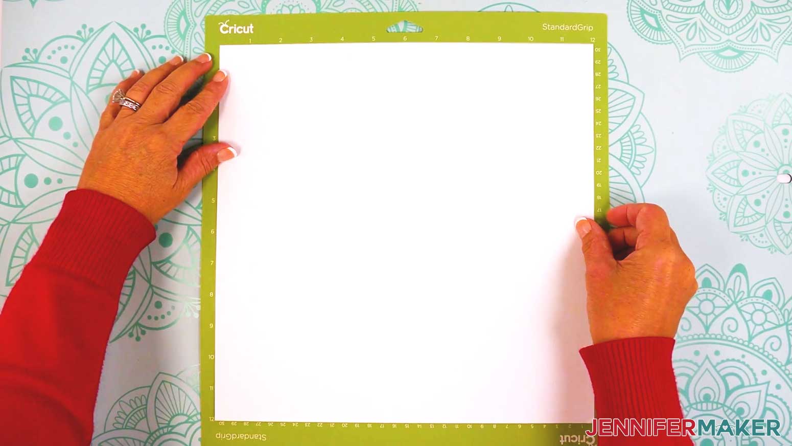 Hands are seen pushing down on a piece of white cardstock to adhere it to the standard, green, Cricut mat.