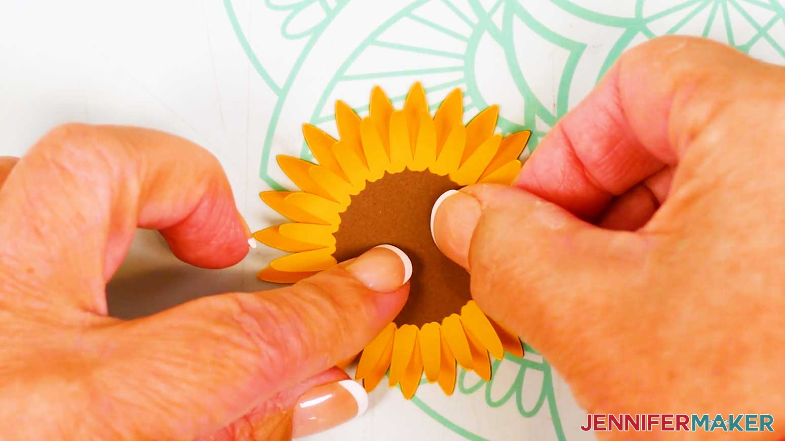 The top and bottom petals of the large sunflower have been glued and the top brown center piece is being glued to the top of them.
