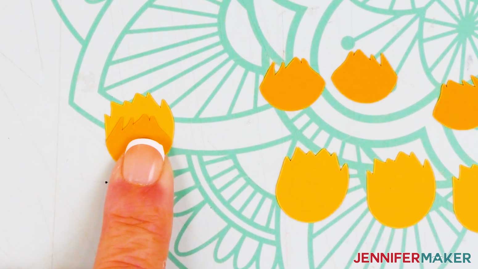 The pieces for the partially open sunflower are arranged on the table and the orange top petals are shown on top of the bottom yellow petal piece.