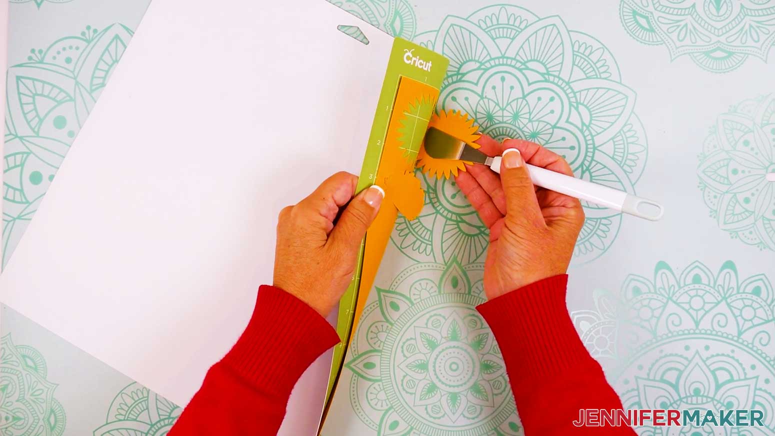 The Cricut mat is rolled around to the back and the spatula is being used to remove the orange delicate flower piece.