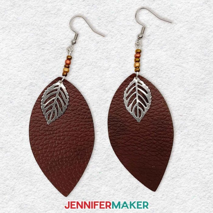 Learn to make easy DIY earrings using faux leather with JenniferMaker's tutorial! A pair of dark brown pebbled faux leather leaf shaped earrings with beaded accent dangles and a silver leaf charm.