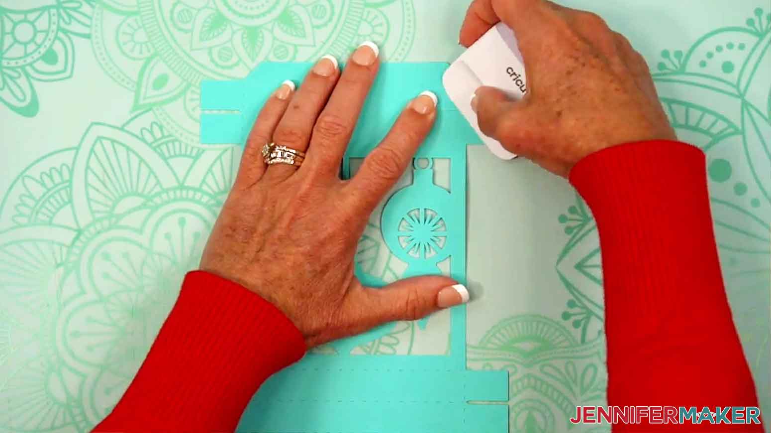 A scraper is being used to help crease the tabs of the lid of the gift box.