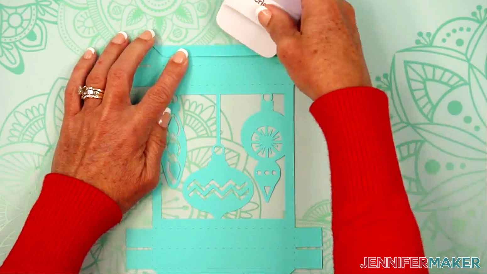 A scraper is being used to help crease the top folding pieces of the gift box.