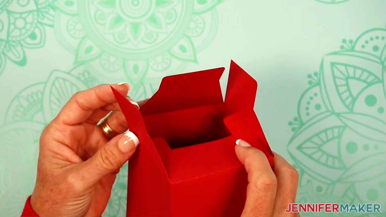 The tumbler gift box is turned upside down and the bottom tabs are being folded down to create a slot for the other tabs.