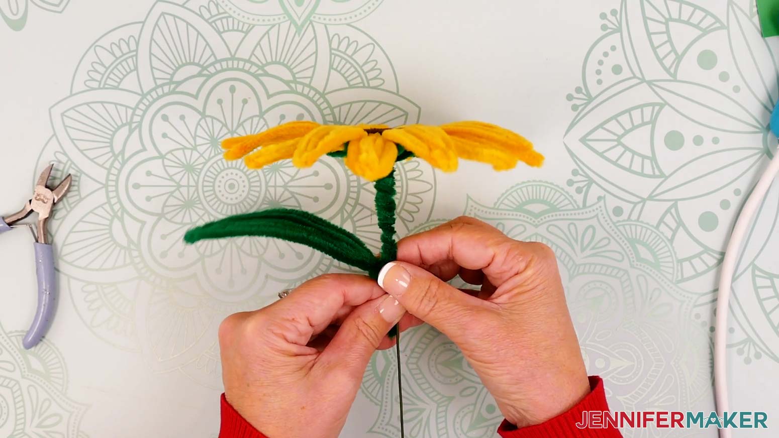 Align the pipe cleaner leaf's joint with the lowest covered stem section so the leaf’s short, loose length is along the bare wire.