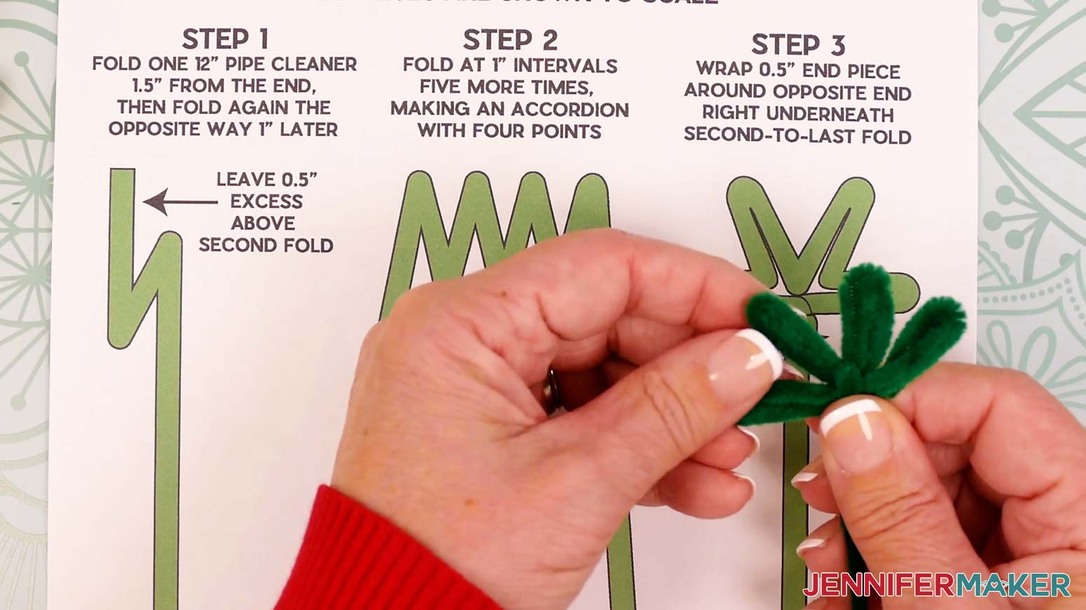 Bring the pipe cleaner’s long end up and between the middle leaves, then make a tight fold to bring it straight back down.