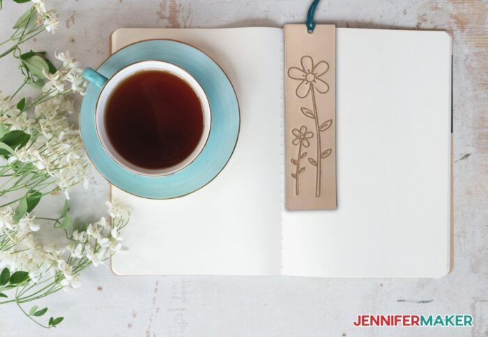 Engraved leather bookmark with floral design on unstained background, holding a journal open.