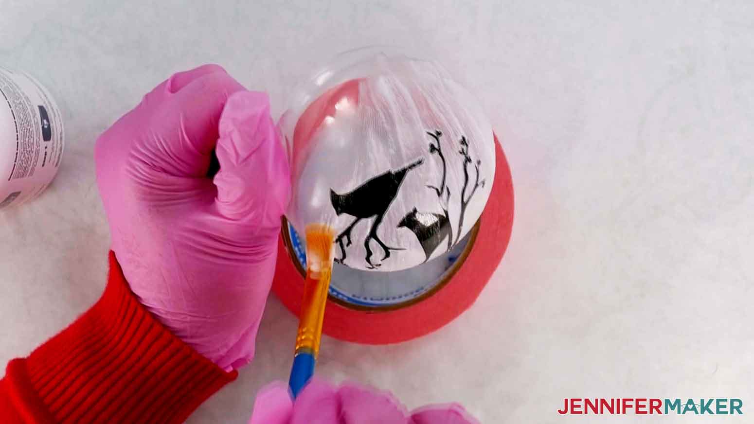 Etching cream being applied with a brush to a glass ornament with a black vinyl cardinal stencil attached