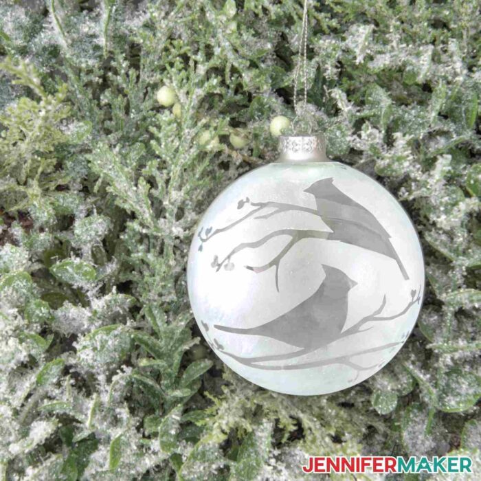Glass ornament etched with cardinal design hanging on pine tree. Make Cricut Christmas Ornaments with JenniferMaker's tutorial!