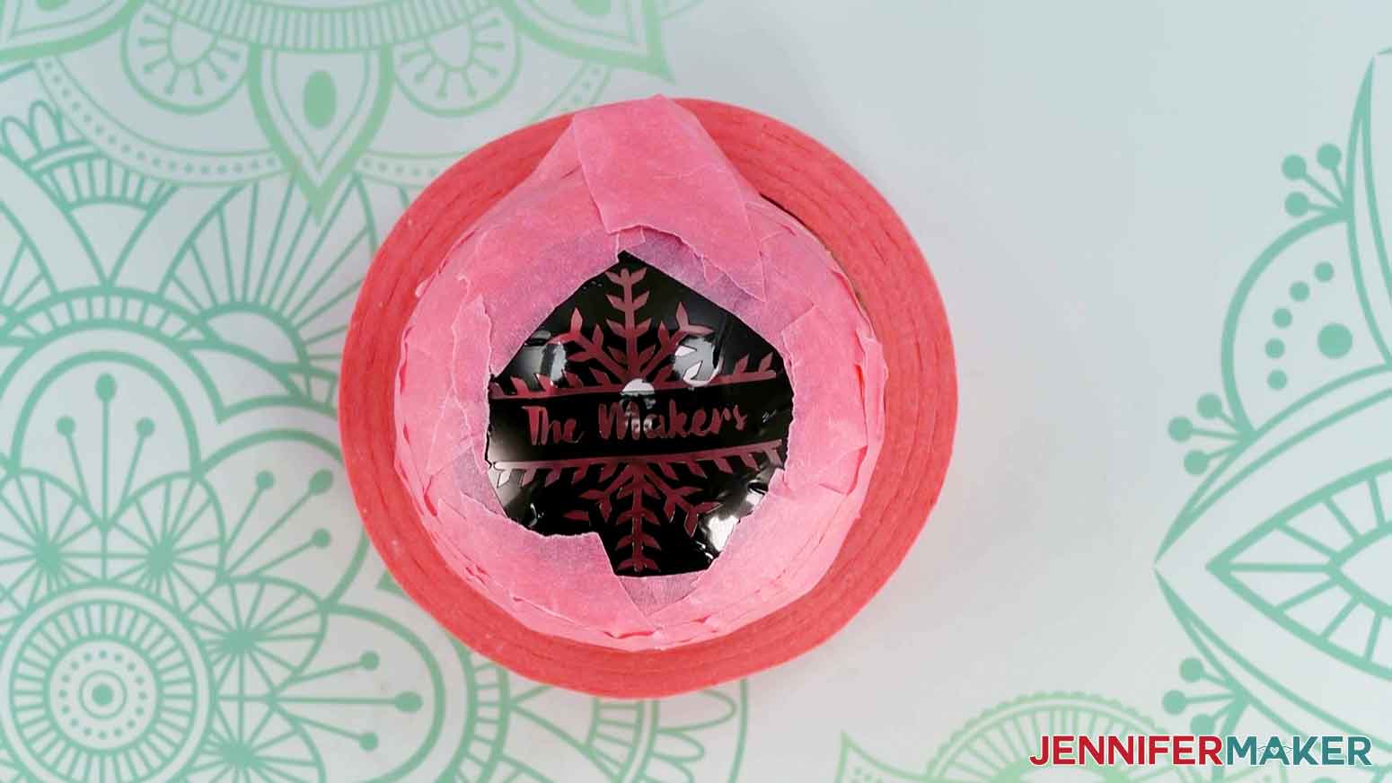 The etched glass ornament snowflake design stencil applied to the front of an ornament with the remaining parts of the ornament covered in pink painter's tape