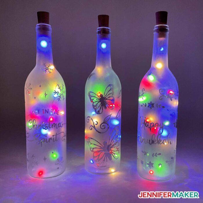 Three etched wine bottles with multicolored lights.