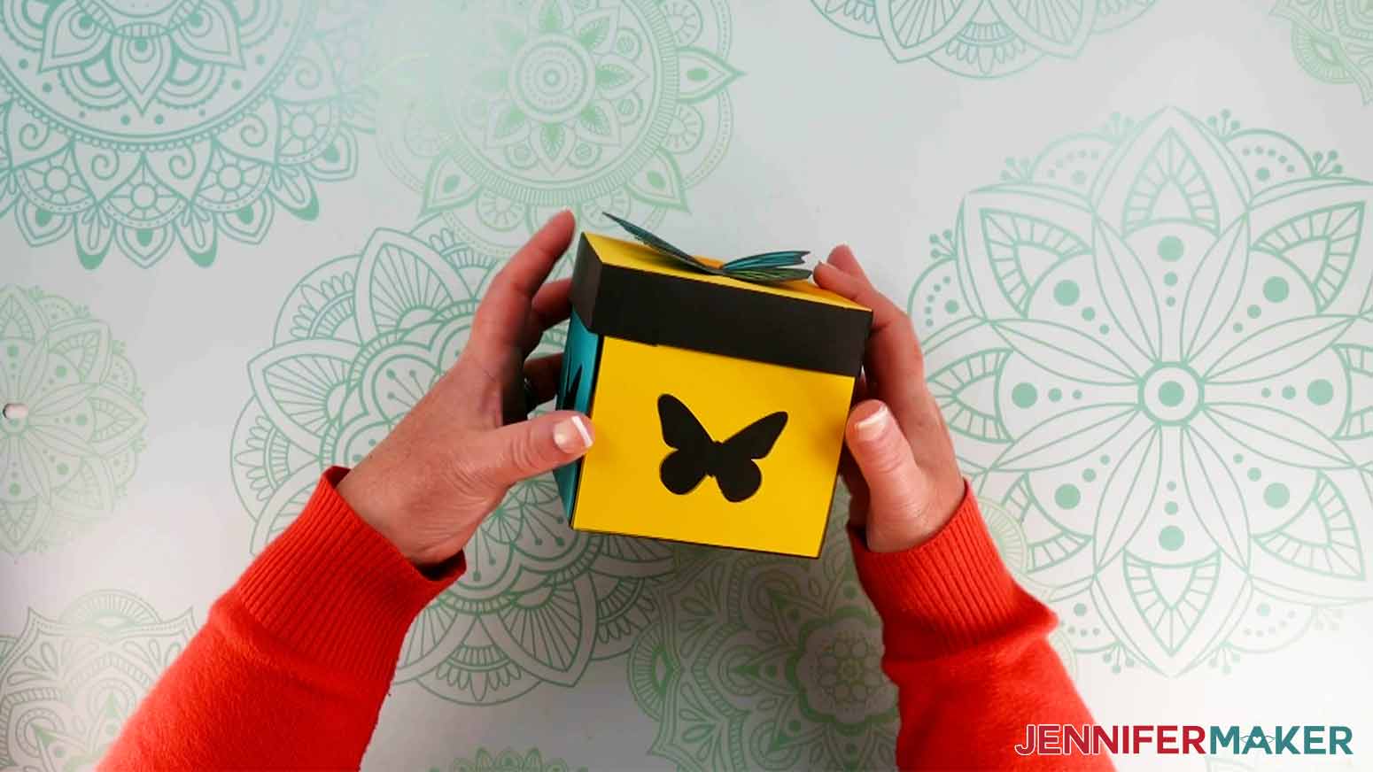 A photo showing two hands holding the finished exploding butterfly box. The colorful side pieces with butterfly cutouts are showing.