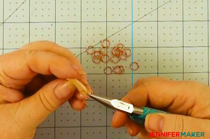 Using needle nose pliers to attach rose gold jump rings to a wood date marker to make a family celebration and birthday board