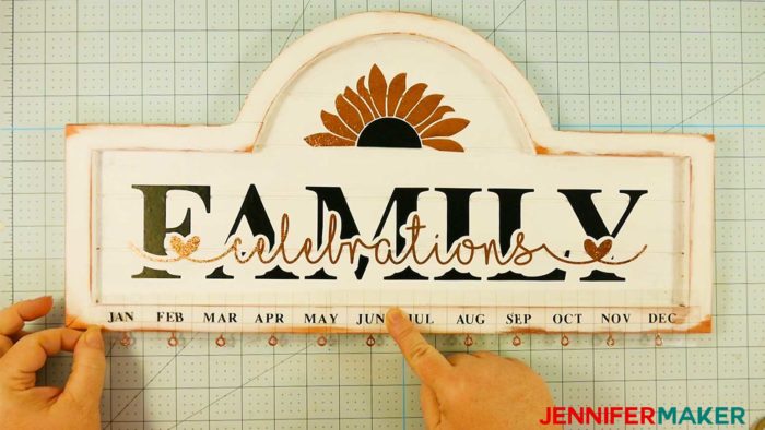 Positioning black vinyl months on the bottom of a family celebration and birthday board