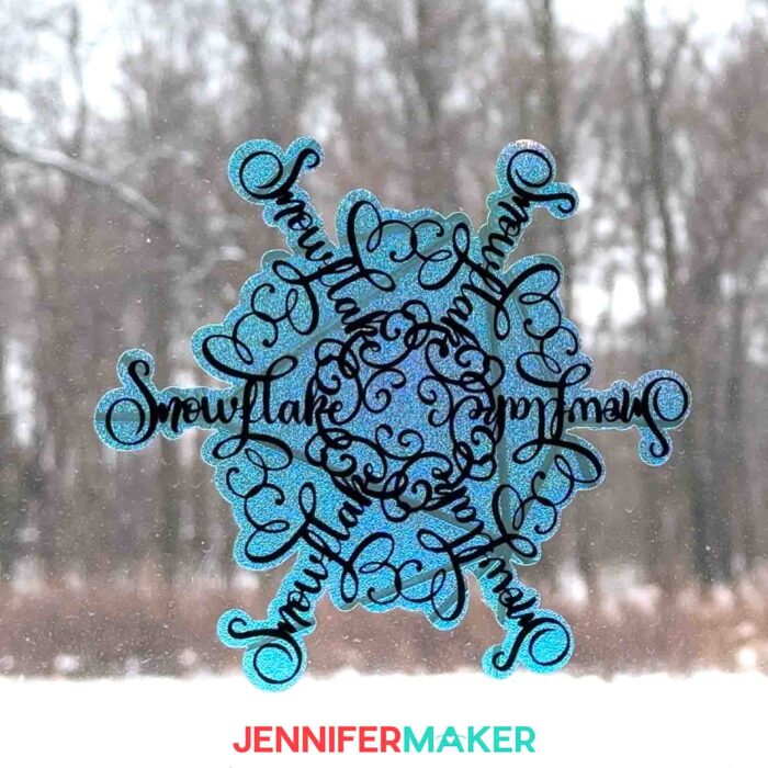 A window from inside the studio at Maker Farm look out onto a snowy landscape -- the windows are decorated with a snowflake-shaped window clings with stylized word art saying "Snowflake" from the Festive Snowflake Designs tutorial