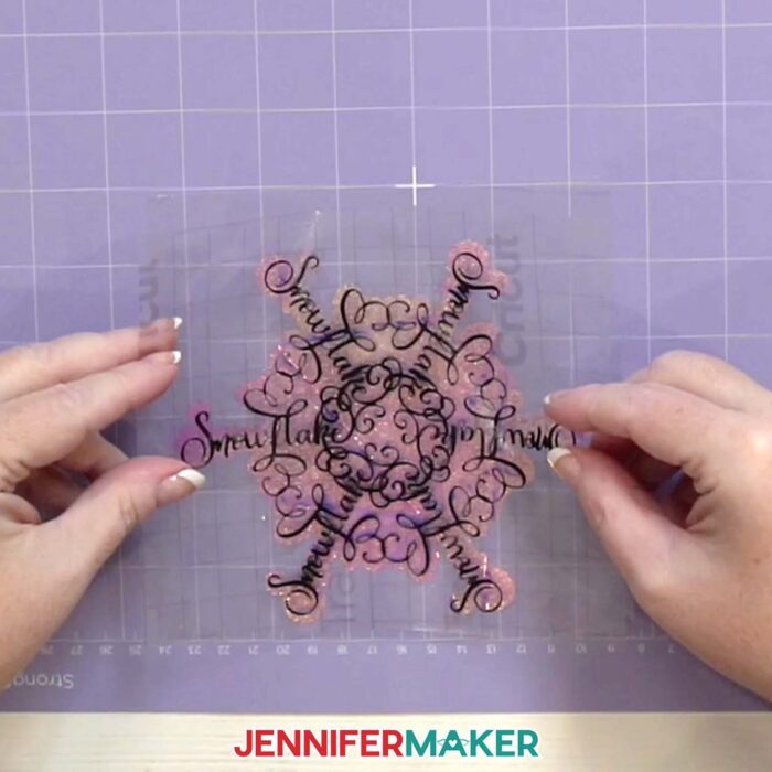 Hands over a purple StrongGrip machine mat place the vinyl snowflake design down onto the cut window cling material in the Festive Snowflake Design Window Cling tutorial