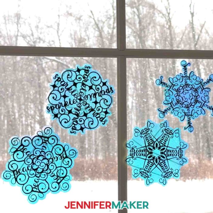 A window from inside the studio at Maker Farm look out onto a snowy landscape -- the windows are decorated with four snowflake-shaped window clings with stylized word art from the Festive Snowflake Designs tutorial