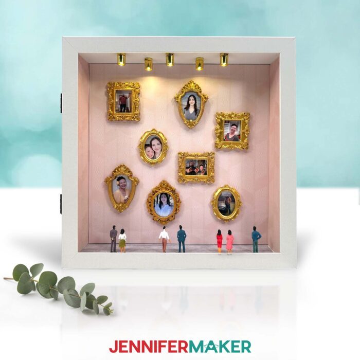 A "Gallery of Us" shadow box on display with mini craft frames on top of photos of Jennifer Maker and her family decorating the box walls, tiny spotlights, and mini figurines facing the photos.