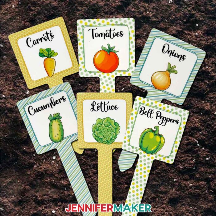 A set of six sublimated plant stakes, each with a photo of a vegetable with its name labeled across the top: "Carrots," "Tomatoes," "Onions," "Cucumbers," "Lettuce," and "Bell Peppers"