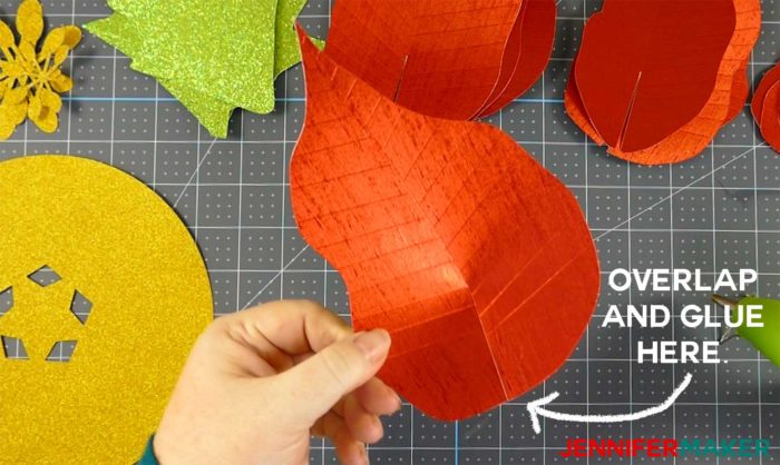 A red foil paper poinsettia leave being glued to create a giant paper poinsettia flower