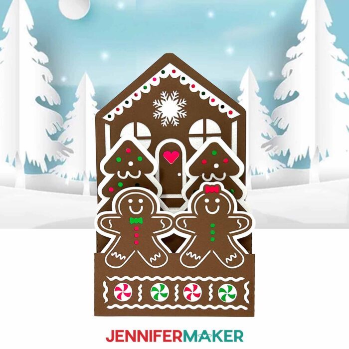A cute brown Gingerbread House Pop-Up Card sits on display, with red, green, and white details and little "cookie" people