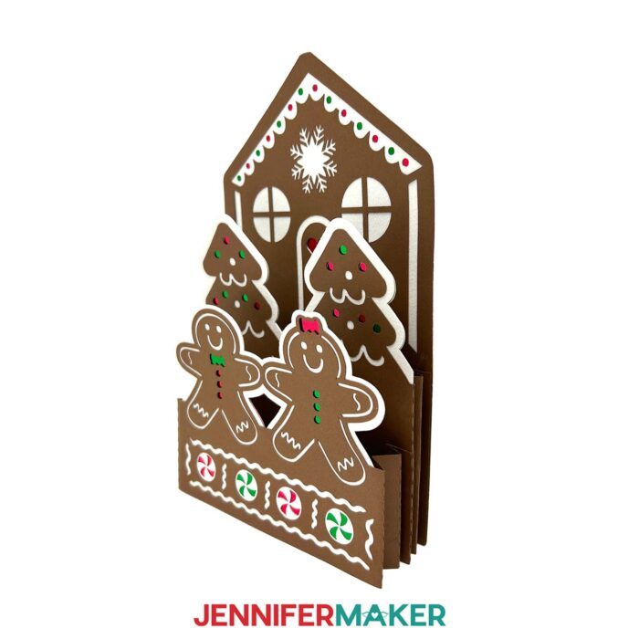 Side view of the Gingerbread House Pop-Up Card sits on display, with red, green, and white details and little "cookie" people