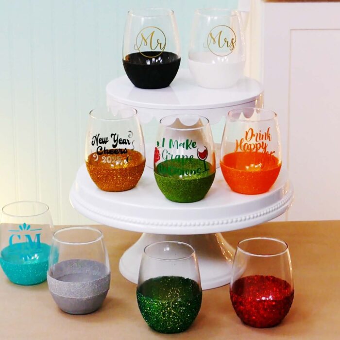 Several stemless glass wine glasses with glitter bottoms and vinyl decals as well as some with just glitter from a tutorial on how to glitter wine glasses.