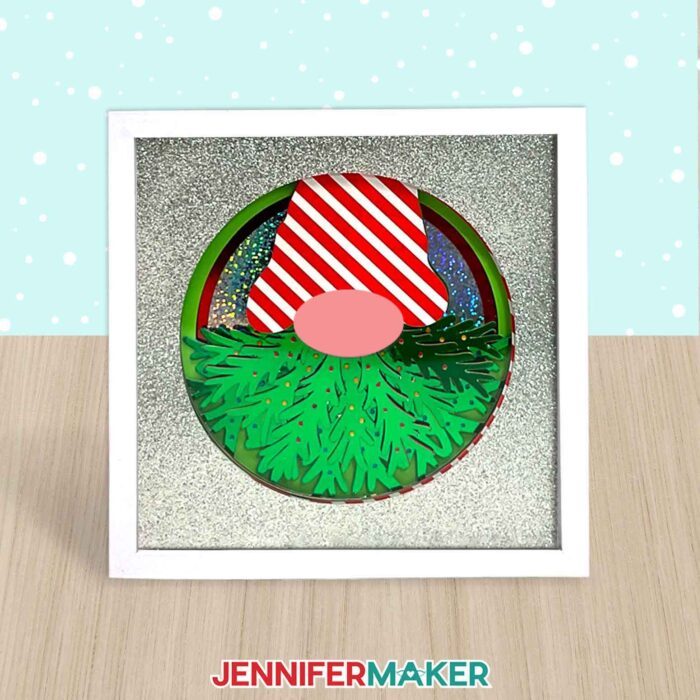 A layered cardstock shadow box gnome with a Christmas tree beard on table. Make this with JenniferMaker's tutorial!