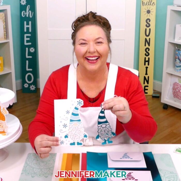 Jennifer Maker sits at her craft studio desk, showing off materials and a card and ornament made from the Gnome Gift Set tutorial