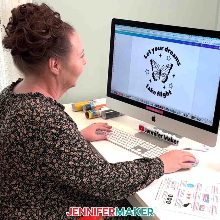 Jennifer Maker sits at her computer designing a butterfly decal that says "Let your dreams take flight" that she made in the Learn How To Create A Cut File In Canva tutorial