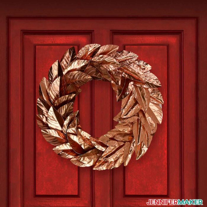 Coppery metal wreath with leaves cut on a Cricut hung on an emerald red front door.