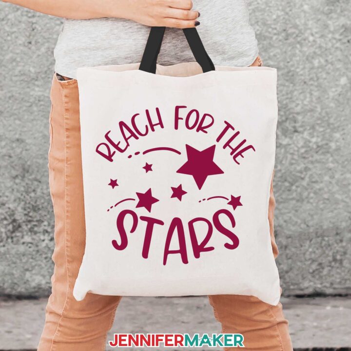 A person holding a white tote bag with reach for the stars in red iron-on vinyl from the how to cut vinyl on Cricut tutorial.