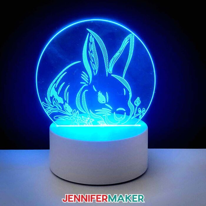Learn how to engrave with a Cricut! A glowing nightlight with an etched rabbit design sits in the dark, lit up with a blue cast. Learn how to engrave with a Cricut with Jennifer Maker's new tutorial!