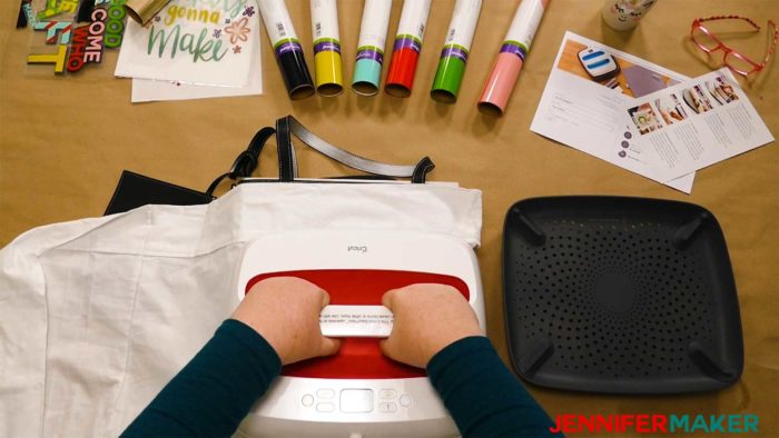 Pressing down on a layered iron on vinyl design on a black tote bag with a Cricut EasyPress 2